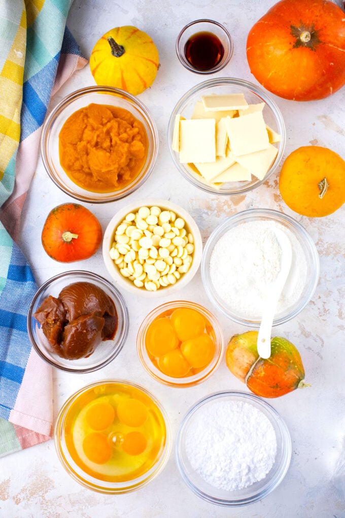 Overhead shot of dulce de leche stuffed pumpkin lava cakes ingredients in bowls on a white surface.
