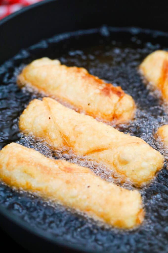 Frying cheeseburger egg rolls in a pan with oil.