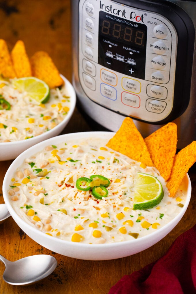 Bowls of Instant Pot white chicken chili served with corn chips and jalapenos.