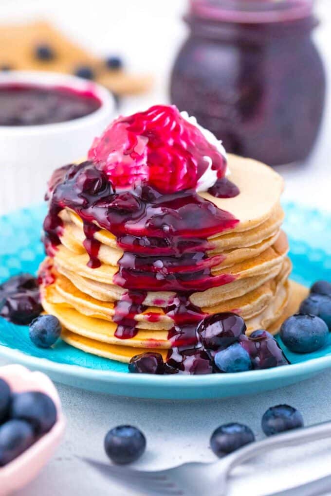 a stack of pancakes topped with homemade blueberry sauce and whipped cream