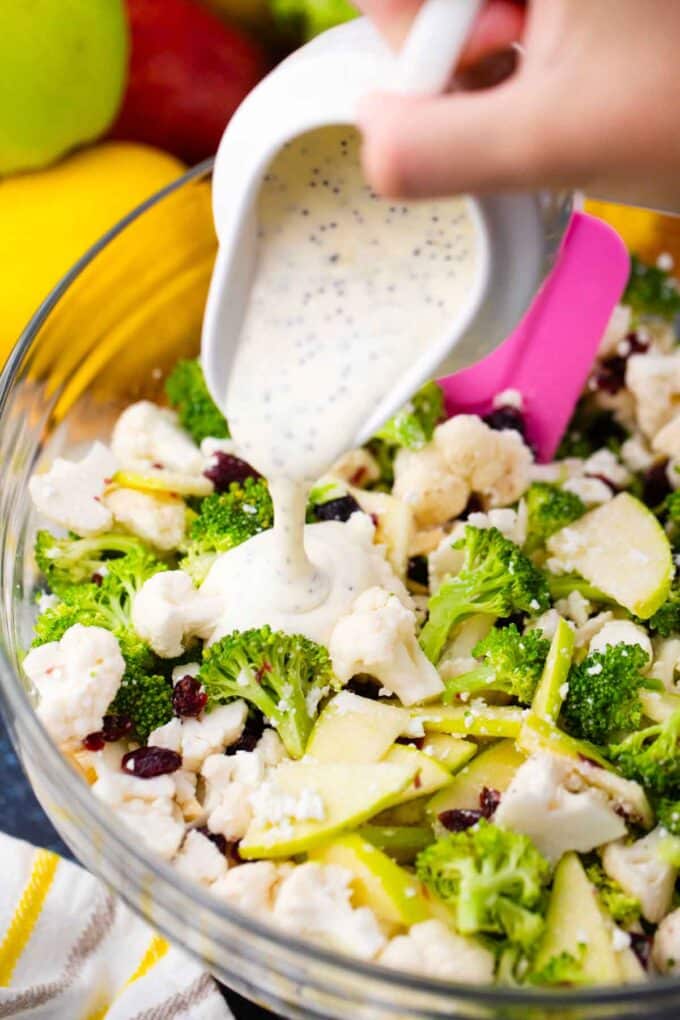 pouring creamy poppy seed dressing on top of broccoli cauliflower salad