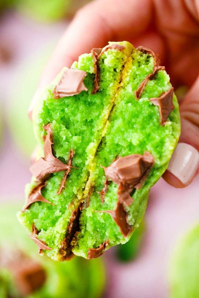 a hand holding a pudding mint chocolate chip cookie halved revealing its chewy center