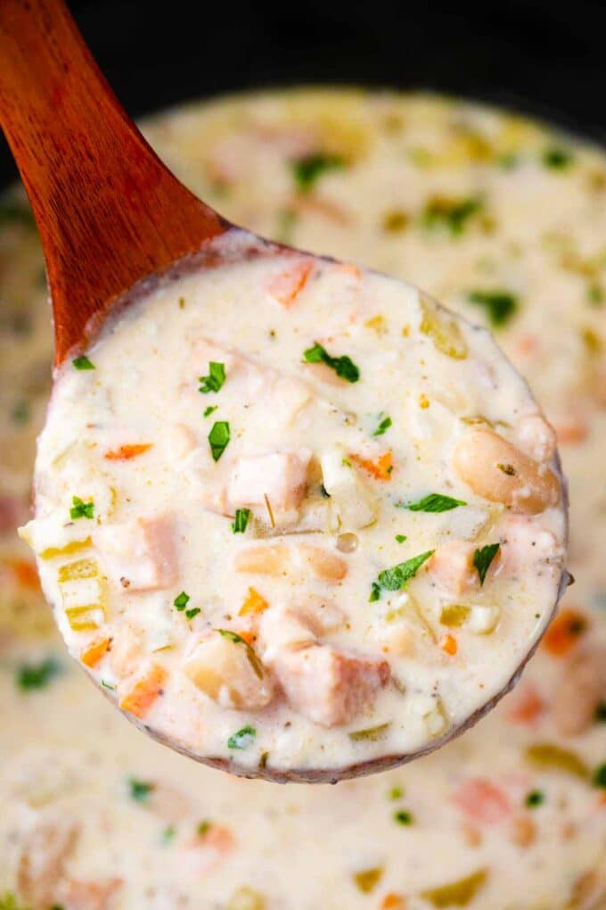 a ladle filled with slow cooker ham and bean soup