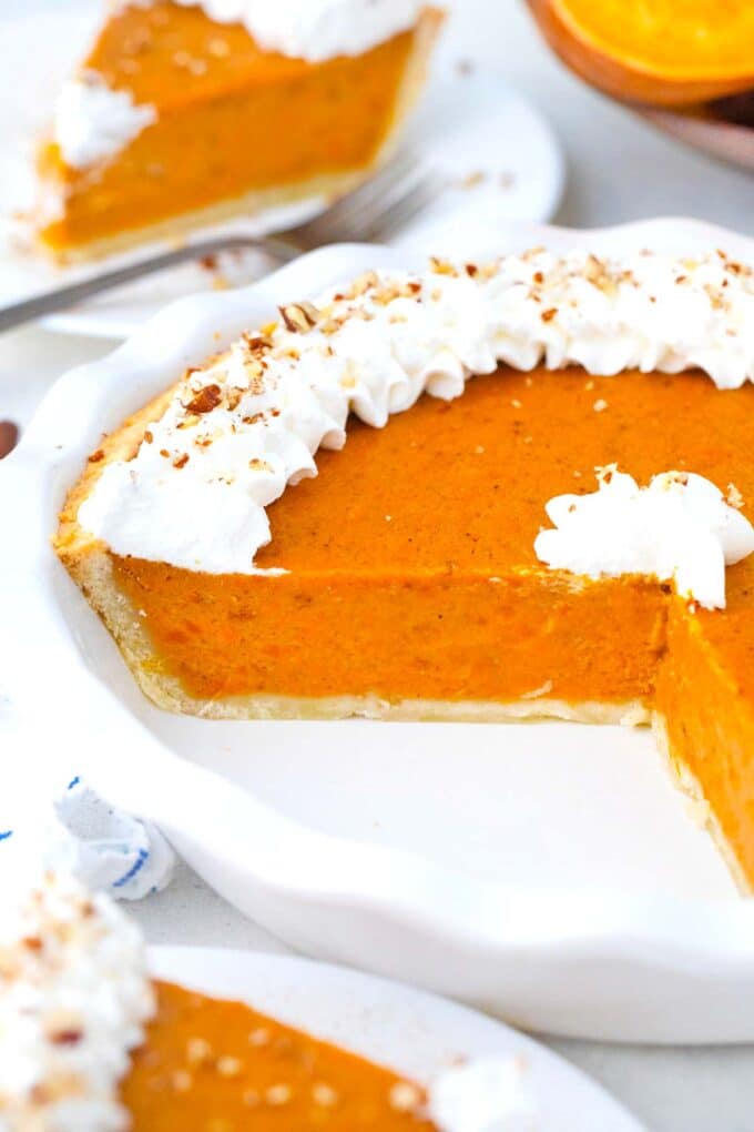 sliced homemade sweet potato pie in a pie dish garnished with whipped cream