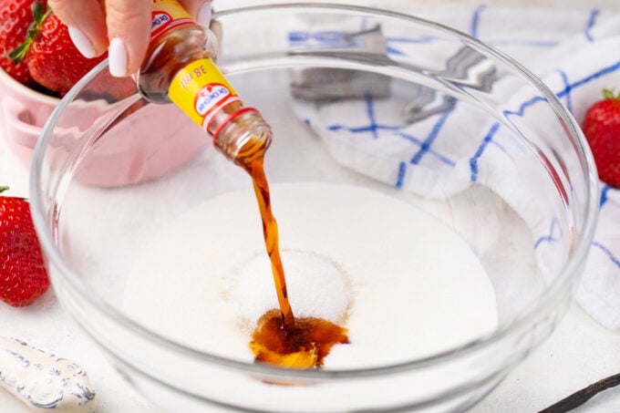 Adding vanilla extract to a bowl with heavy cream and sugar.