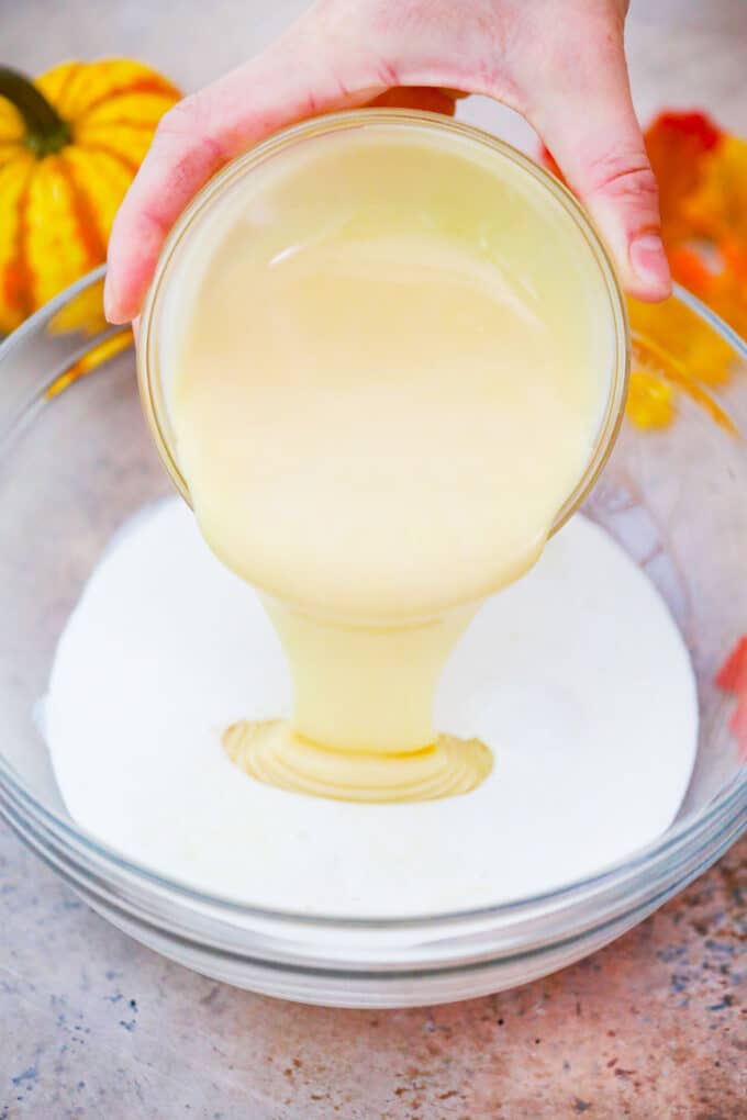 Pouring condensed milk into a bowl with evaporated milk.