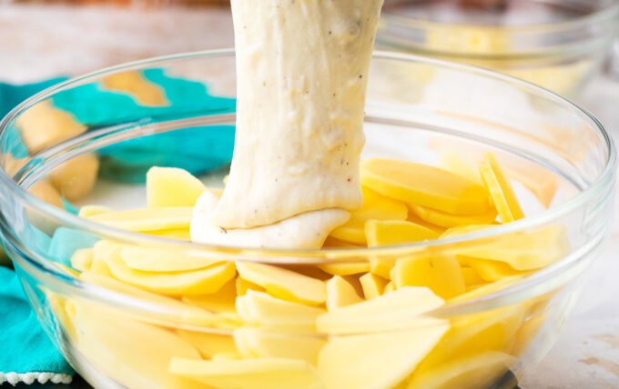 Adding cheesy sauce to thinly sliced potatoes to make bechamel sauce potato gratin.