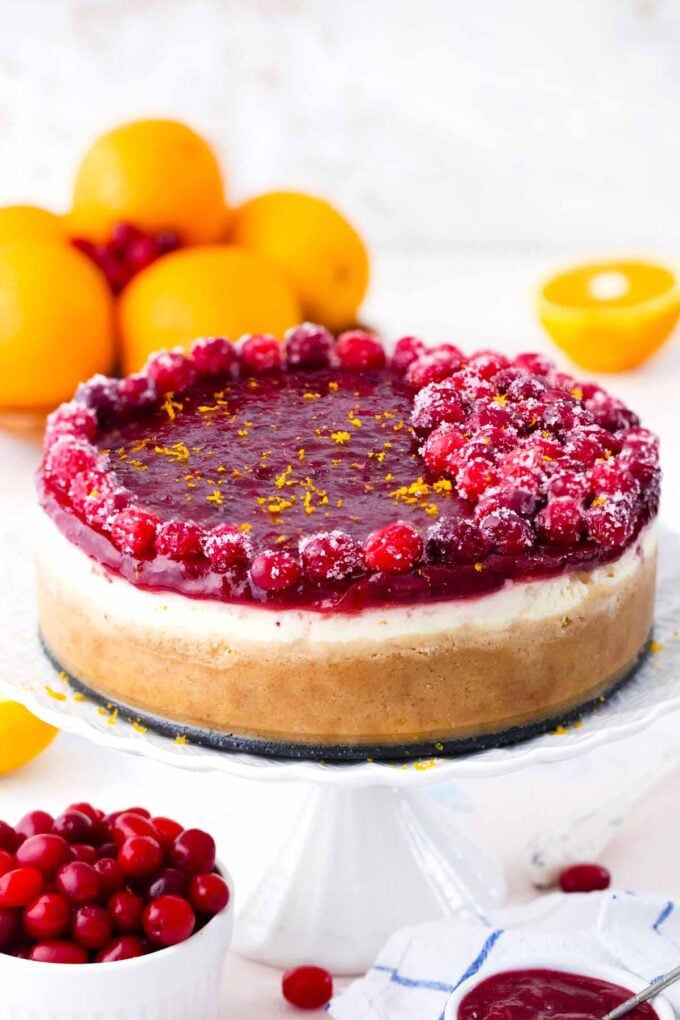 orange cranberry cheesecake on a cake stand with oranges and cranberries next to it