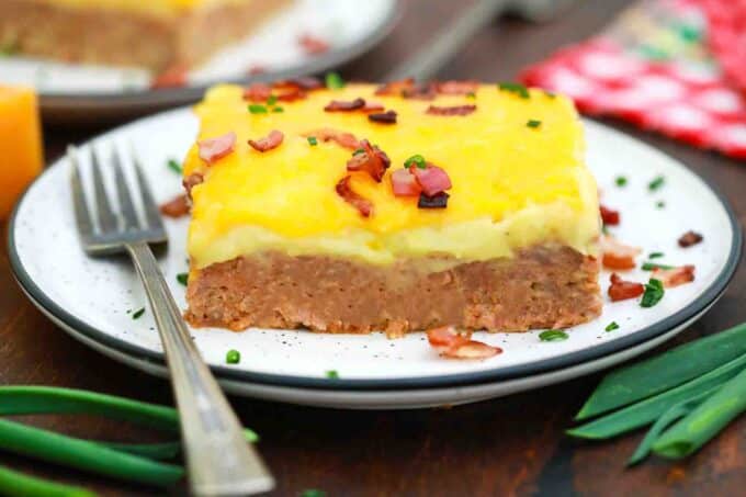 a plate with a slice of potato and meatloaf casserole topped with crispy bacon
