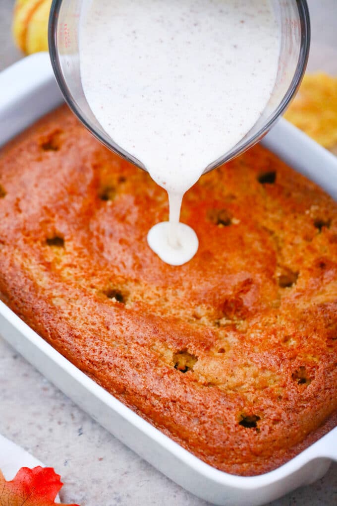 Pouring tres leches mixture over poked pumpkin cake.