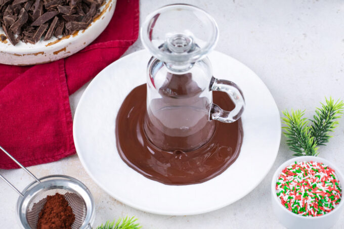 Dipping the rim of a glass cup in melted chocolate.