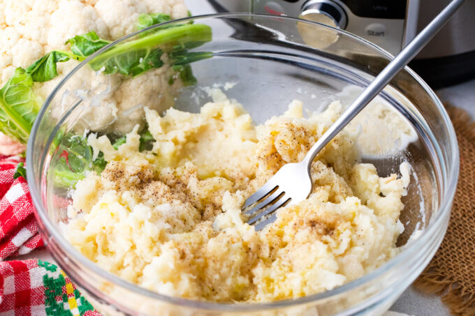 Mashing cooked cauliflower in a bowl.