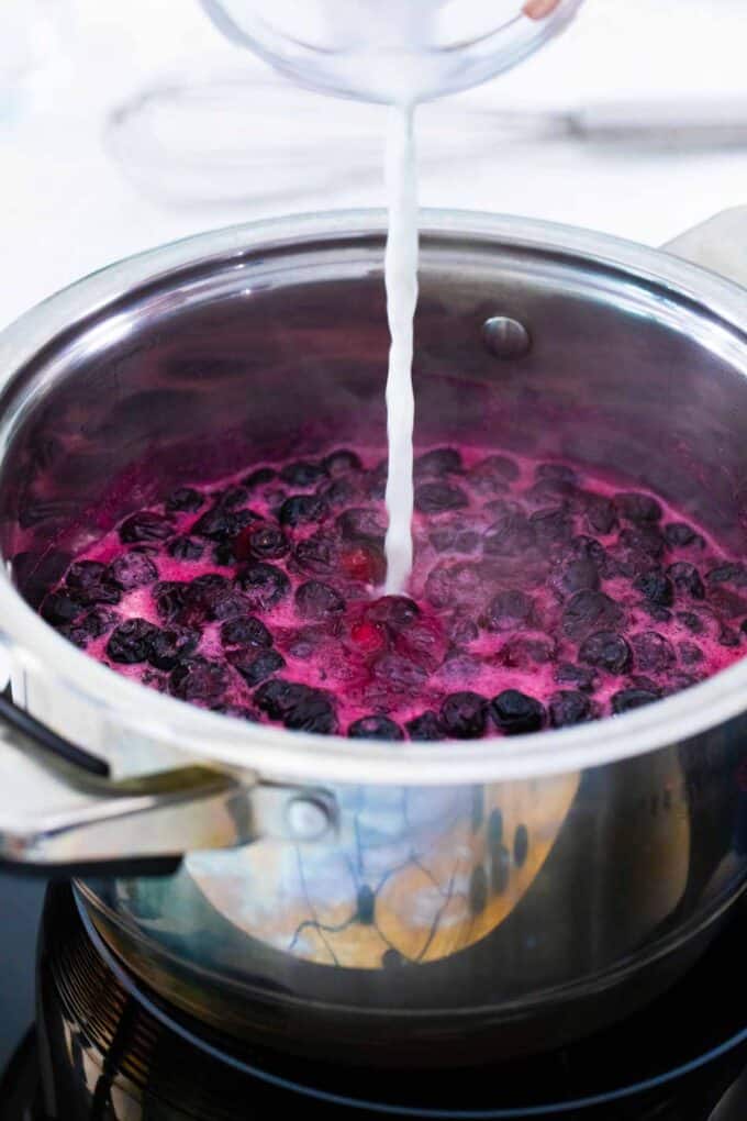 adding cornstarch slurry to homemade blueberry sauce in a sauce pan