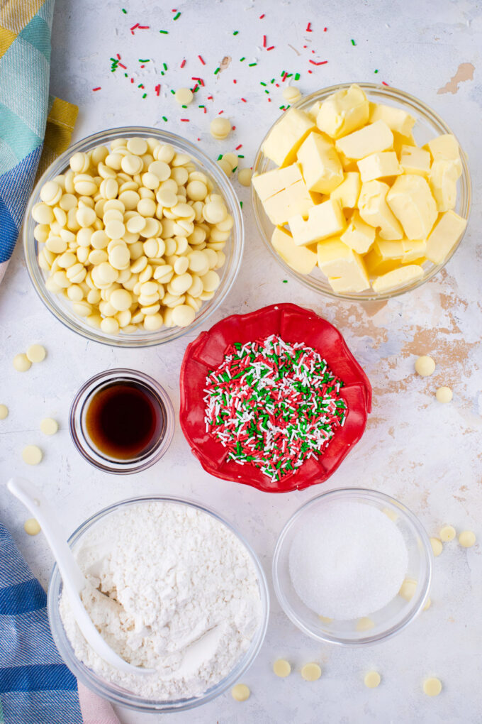 Overhead shot of sugar cookie truffles ingredients in bowls on a white surface.