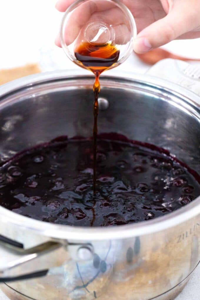 adding vanilla extract to homemade blueberry sauce in a sauce pan