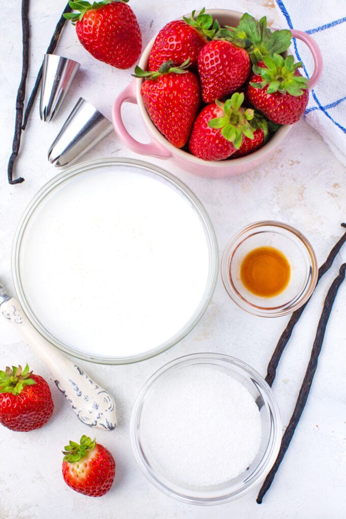 Overhead shot of whipped cream ingredients in bowls on a white surface.