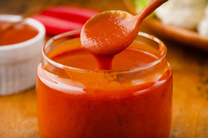 Buffalo sauce dripping of a spoon into a jar.