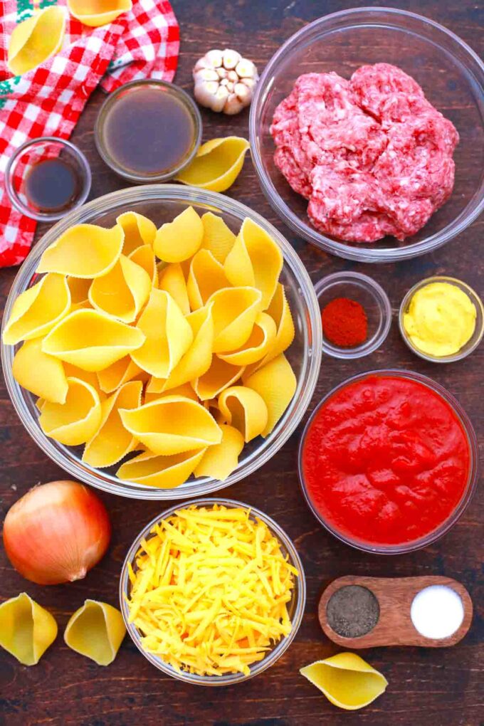 overhead shot of pasta shells ground beef cheese tomato sauce and spices in bowls on a table