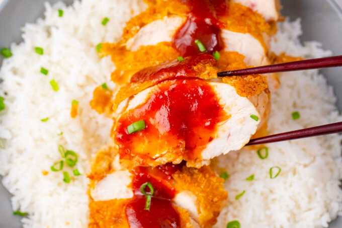 Holding with chopsticks a piece of crispy chicken katsu covered in tonkatsu sauce.