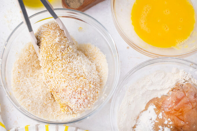 Tossing chicken breast in Panko breadcrumbs.