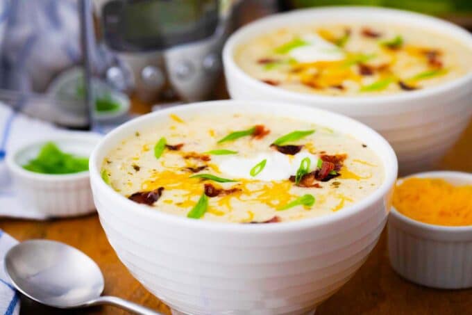 two bowls of crockpot cheesy potato soup topped with bacon and cheese