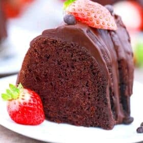 a slice of chocolate pound cake topped with chocolate ganache and fresh strawberries