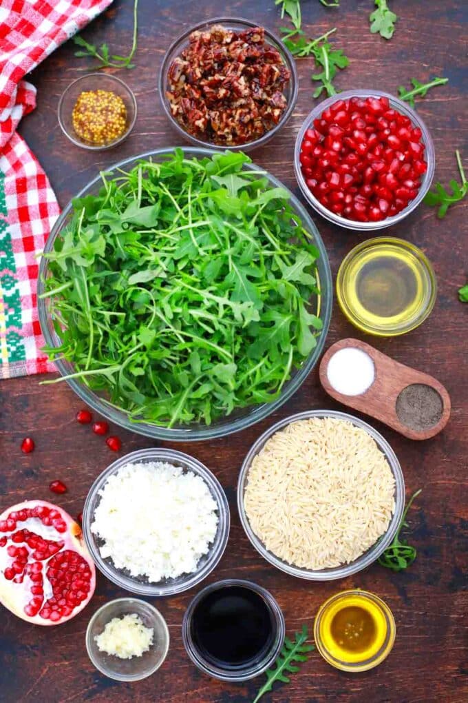 overhead shot of arugula pomegranate seeds orzo feta cheese in bowls on a table