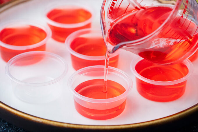 Pouring boozy jello into small plastic cups.