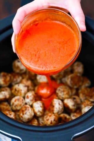 adding buffalo sauce to chicken meatballs in the slow cooker