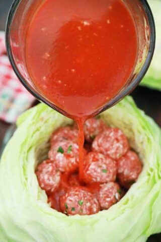 pouring tomato sauce over meatballs in a cabbage