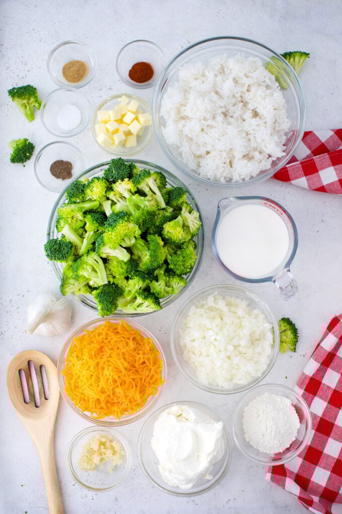 Overhead shot of cheesy broccoli rice casserole ingredients in bowls on a white surface.