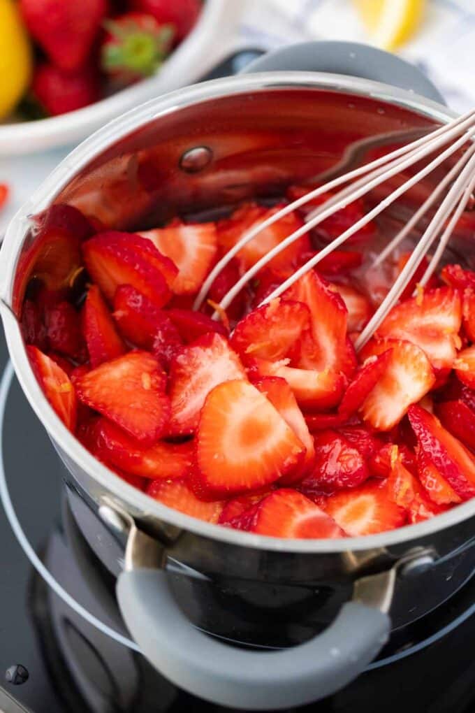 Whisking sliced strawberries in a saucepan.