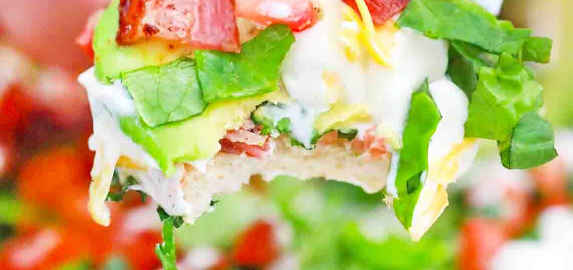 scooping BLT dip with avocado lettuce and tomatoes