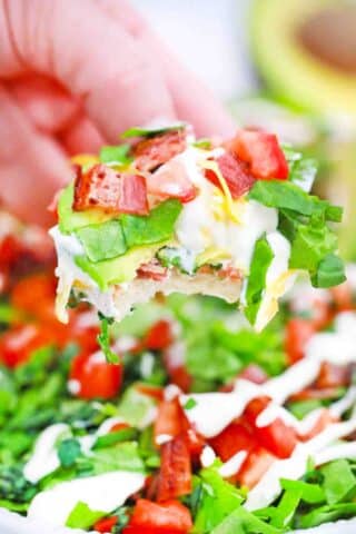 scooping BLT dip with avocado lettuce and tomatoes