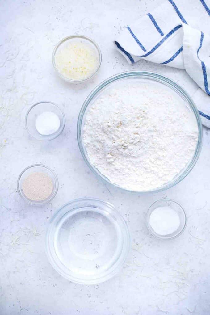overhead shot of flour instant yeast salt sugar and water in bowls on a table