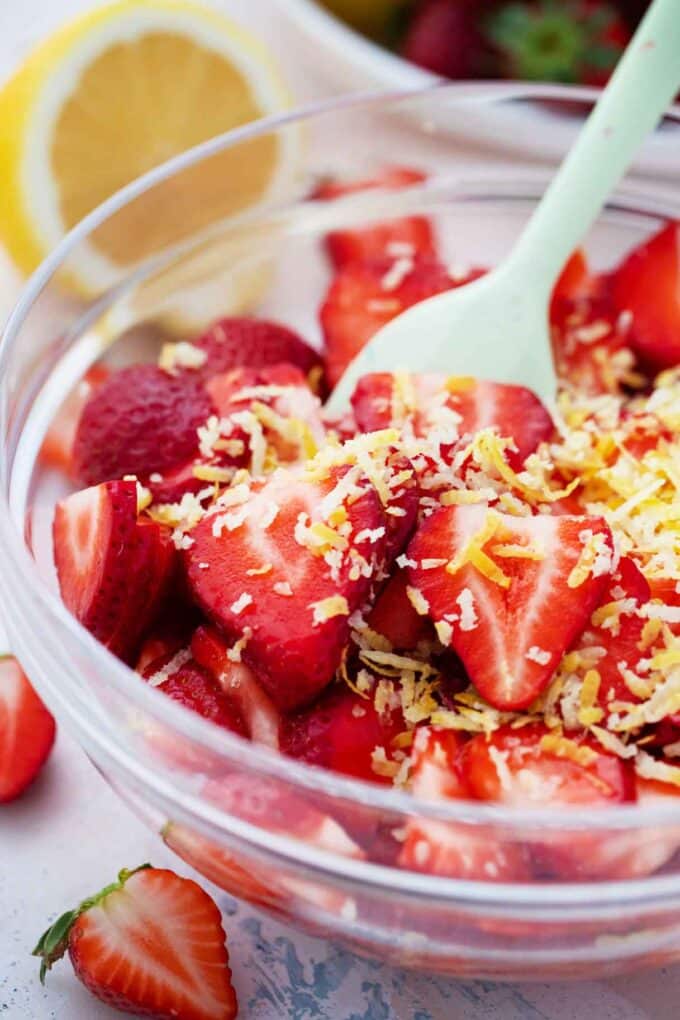 Mixing sliced strawberries and lemon zest in a bowl.