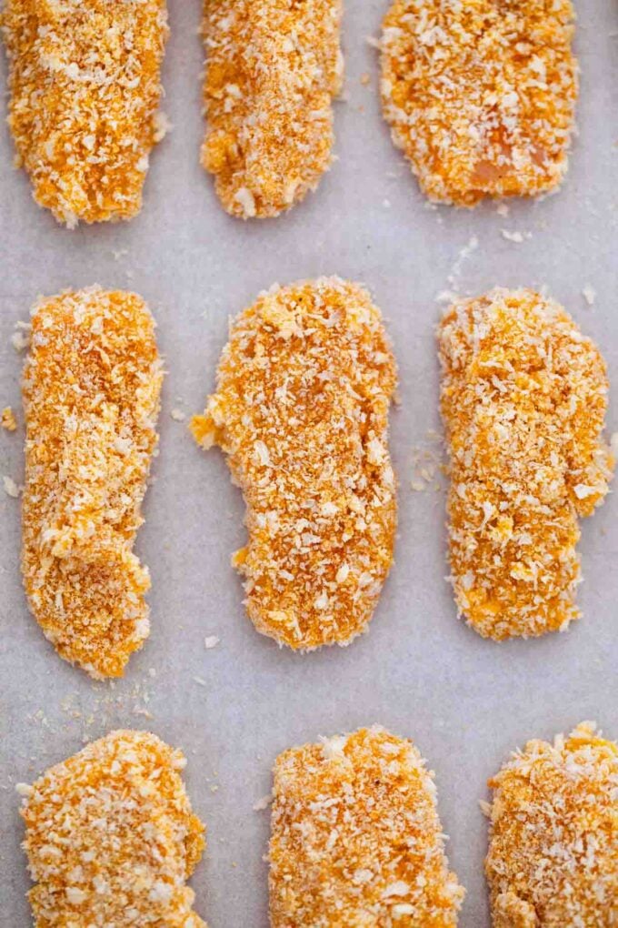 breaded chicken tenders layered on a baking sheet