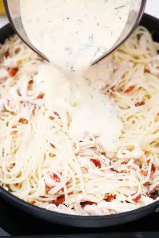 pouring creamy carbonara sauce over pasta