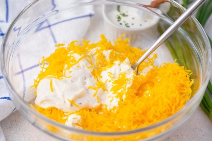 Mixing cream cheese with cheddar cheese in a bowl.