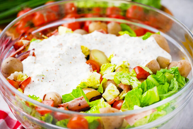 Adding a creamy dressing to BLT potato salad.