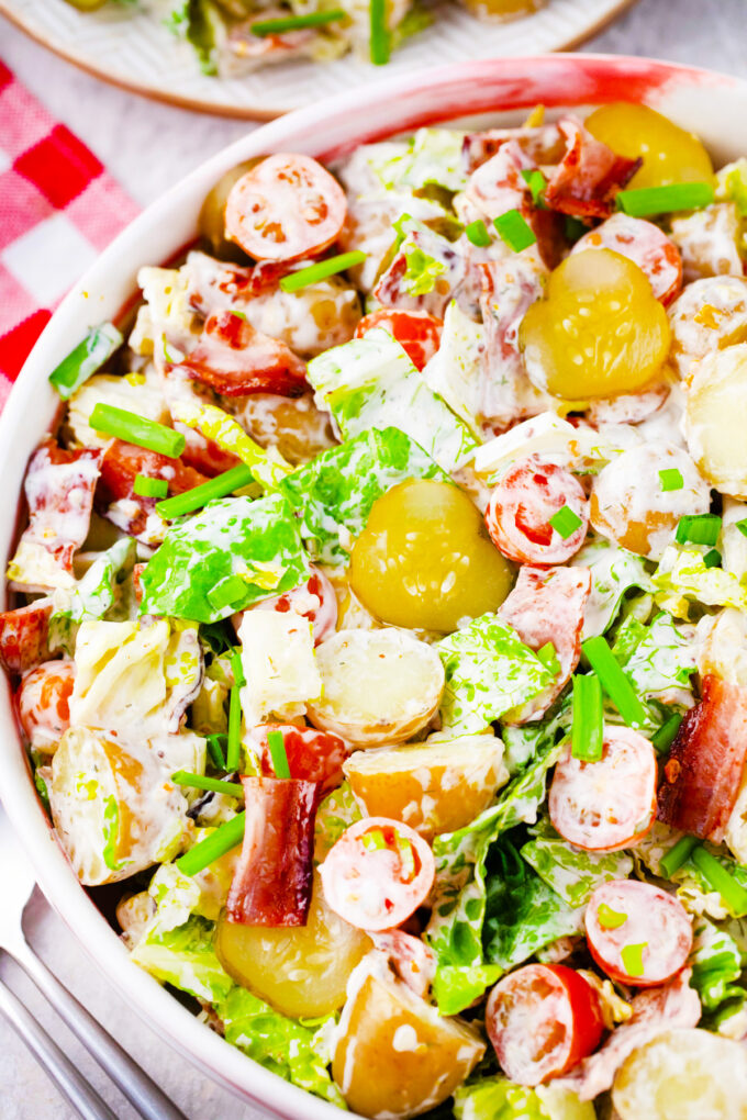 A bowl of BLT potato salad with pickle slices.
