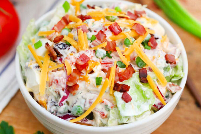 A bowl of overnight salad with creamy buttermilk dressing and shredded cheese.