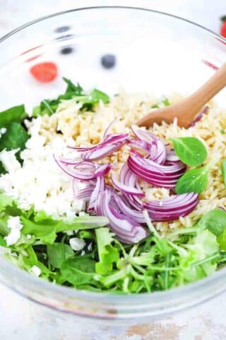 adding orzo onions and feta to spring greens mix