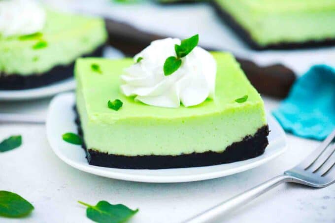 oreo mint cheesecake bars with whipped cream and fresh mint leaves and a blue towel in the background