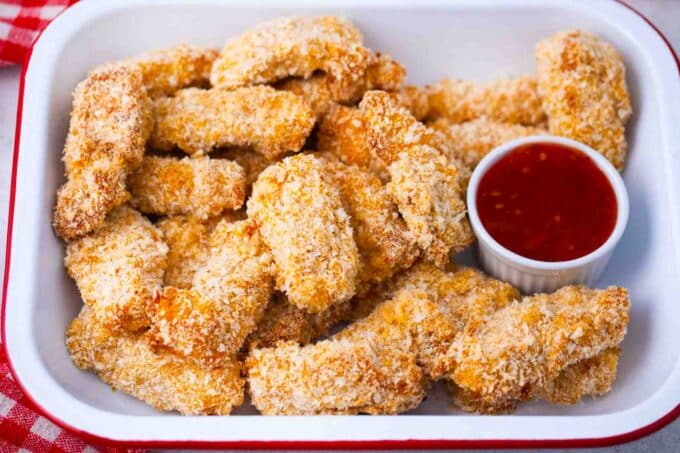 a large tray with crispy oven baked chicken tenders and a dipping bowl of ketchup