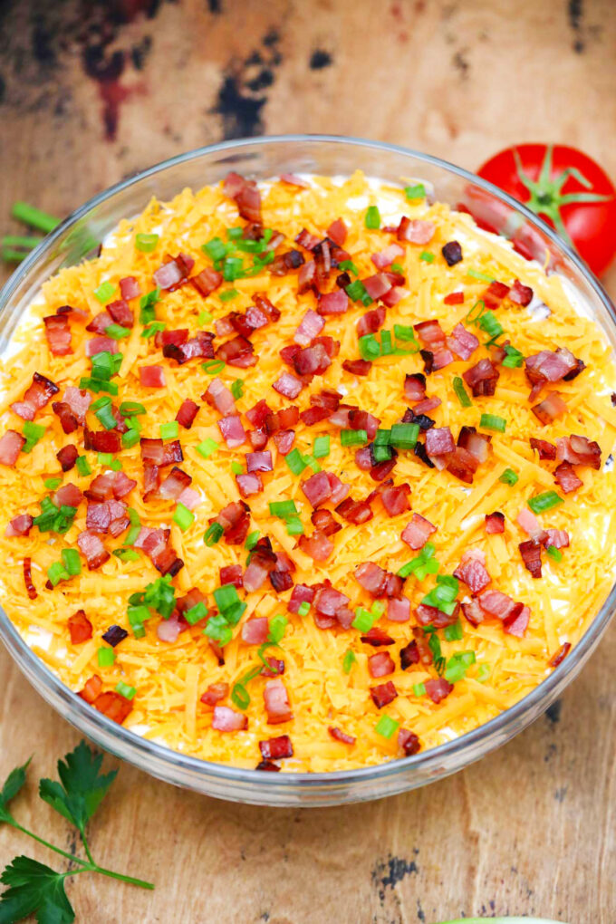 Overhead shot of creamy seven layer salad topped with bacon and shredded cheese.