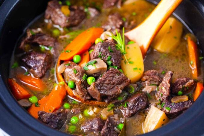 a ladle of slow cooker lamb stew with carrots, potatoes, peas and rosemary