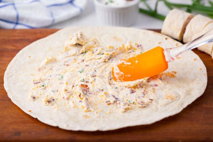 Spreading cream cheese mixture onto a tortilla.