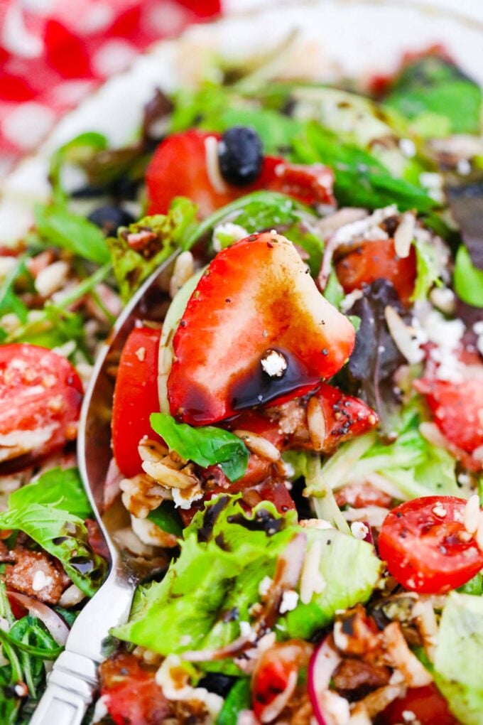A spoonful of strawberry orzo salad with mixed greens, feta, and bacon.