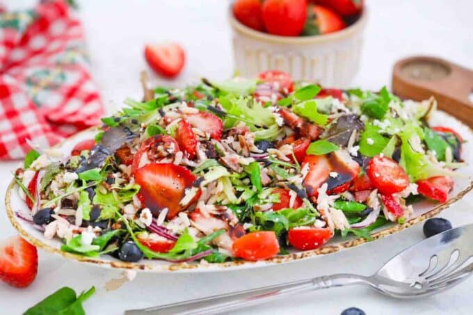 a platter of strawberry orzo spring salad with a bowl of strawberries in the background